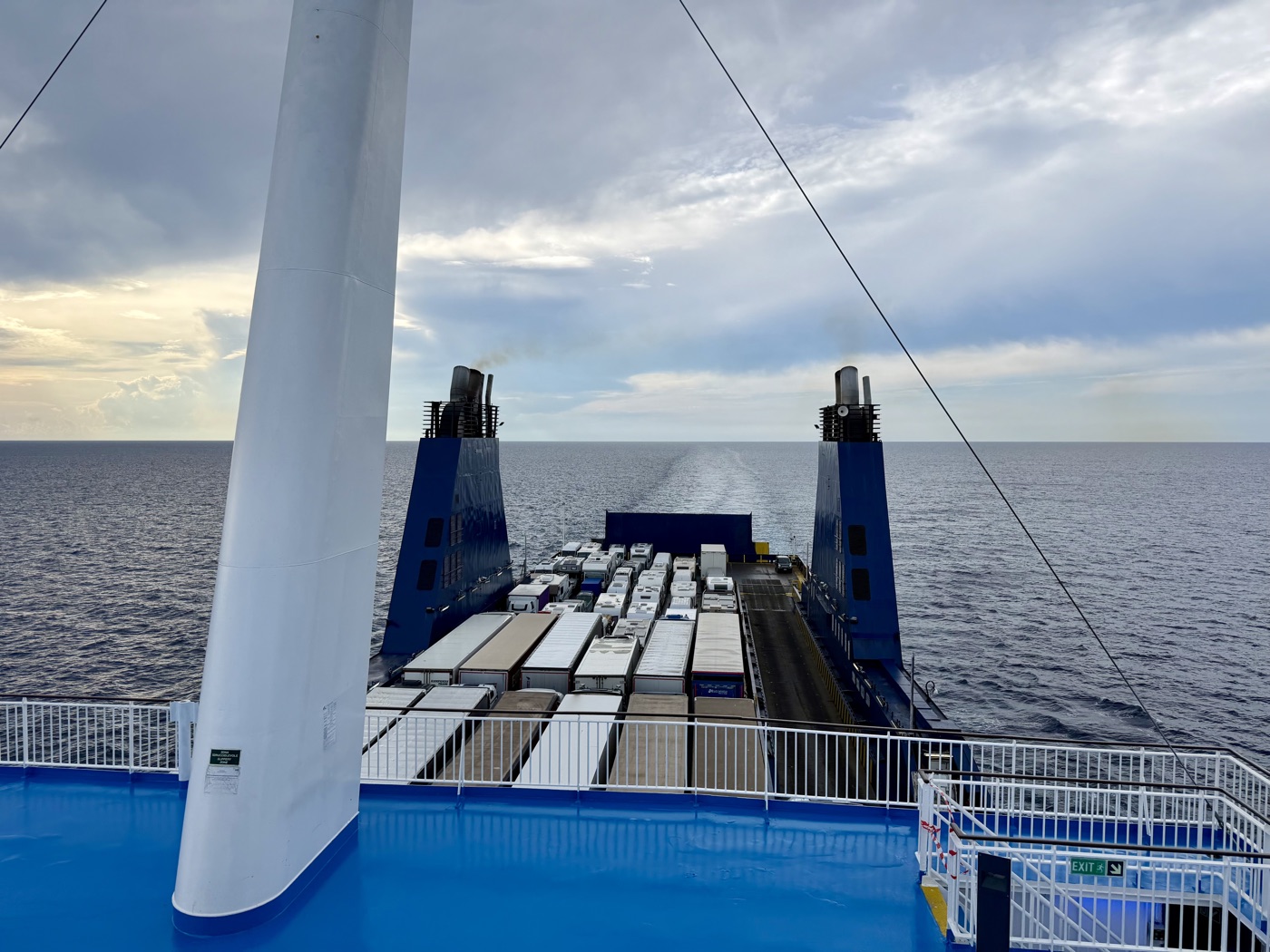 Blick vom Oberdeck der Fähre über die Heckrampe auf viele geparkte Lastwagen und das offene Meer