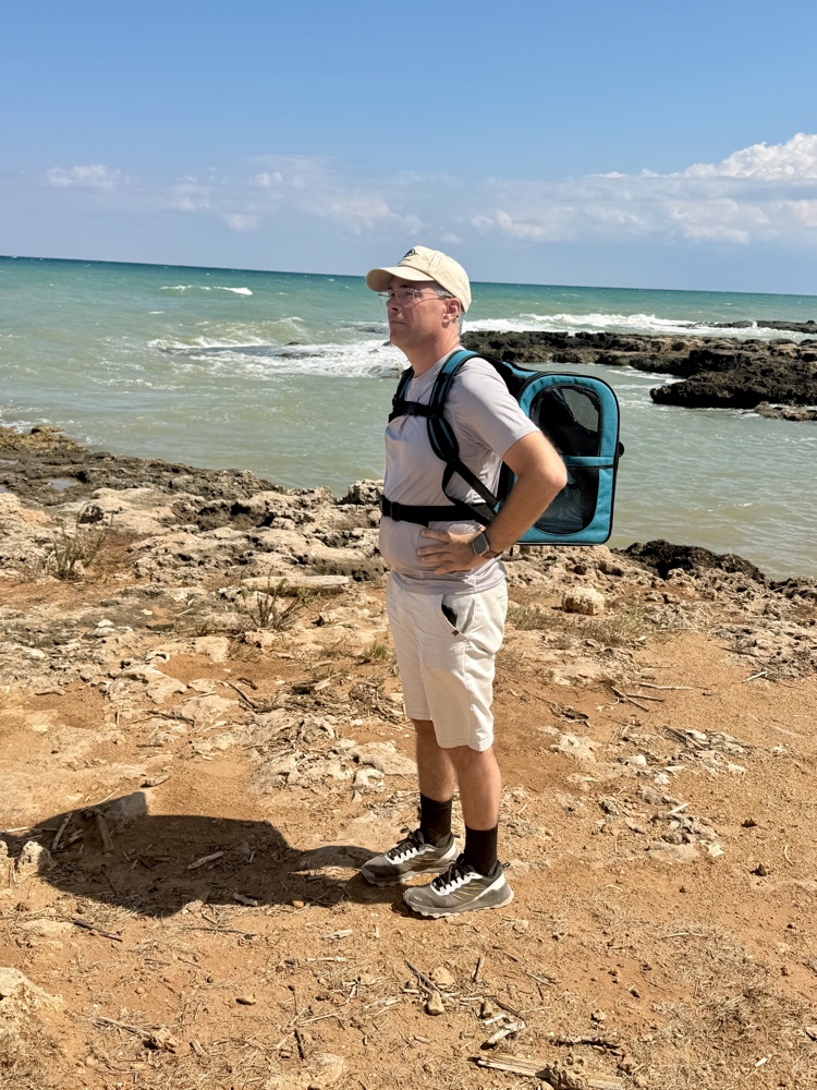 Sven mit Rucksack und Kappe steht auf den Felsen am türkisfarbenen Meer