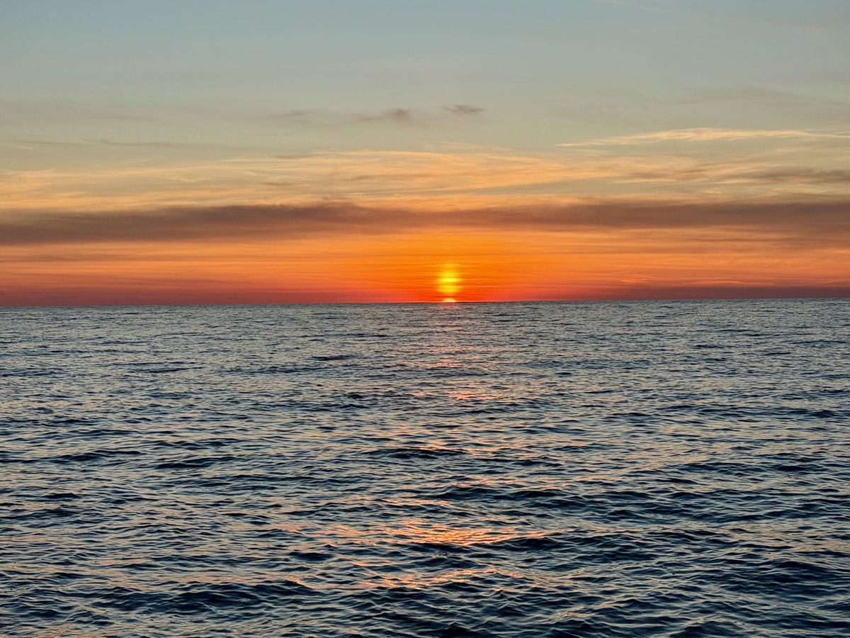 Orangefarbener Himmel und die tiefstehende Sonne über dem dunkelblauen Meer