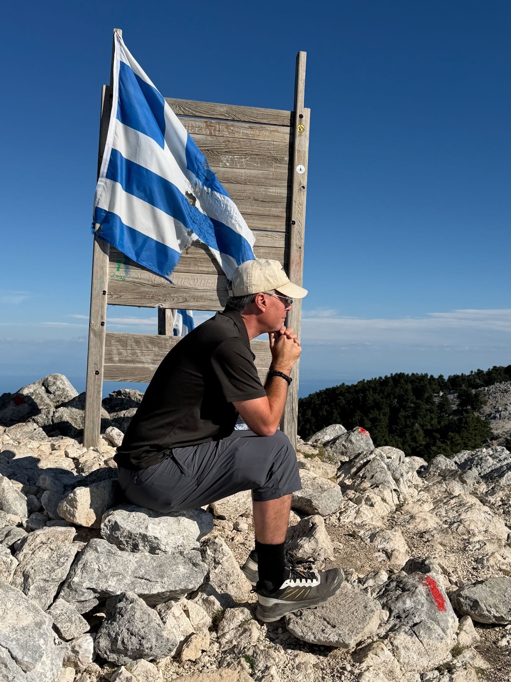 Ein Wanderer kniet auf dem Gipfel vor einer griechischen Flagge