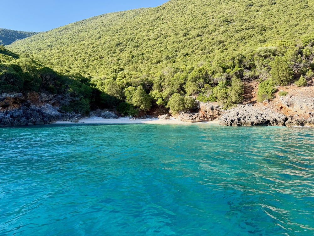 Einsame Bucht mit hellem Strand und türkisfarbenem Wasser vor grünen Hängen