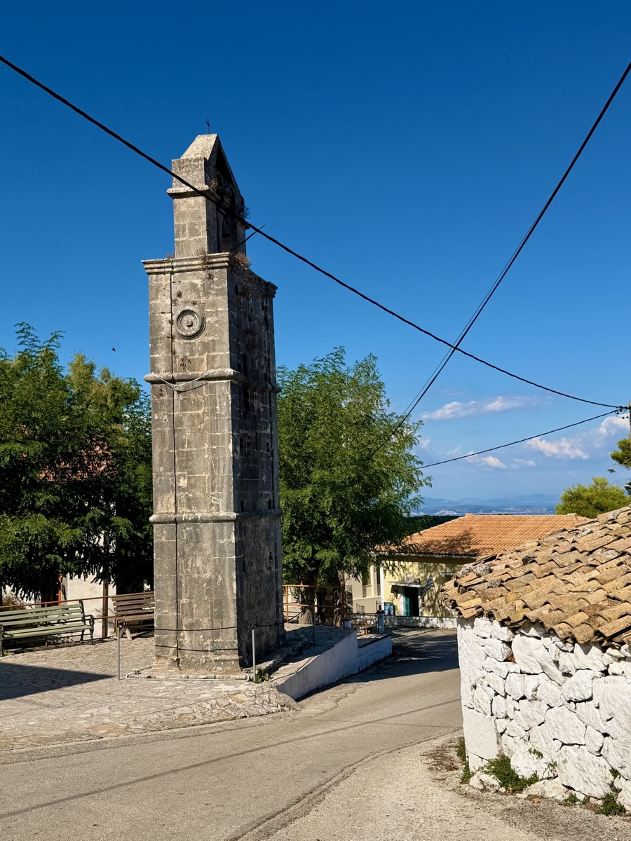 Schmaler steinerner Glockenturm an einer Straße unter blauem Himmel