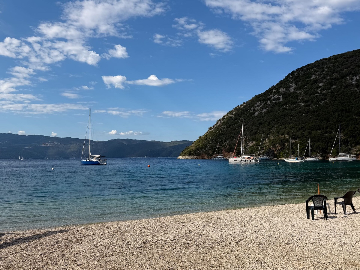 Kieselstrand mit zwei Stühlen und Segelbooten in einer Bucht
