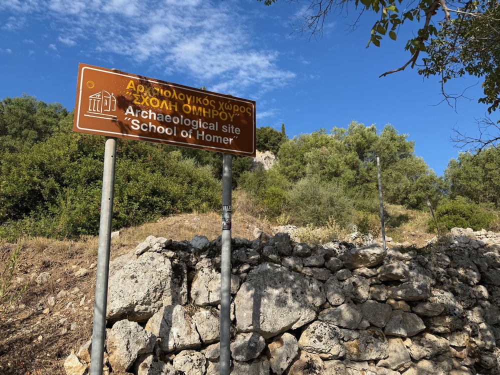 Braunes Schild mit der Aufschrift Archaeological site School of Homer vor einer Steinmauer