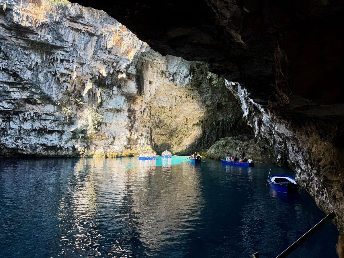 Blick über das dunkle Wasser der Höhle auf mehrere Boote und eine Felsöffnung
