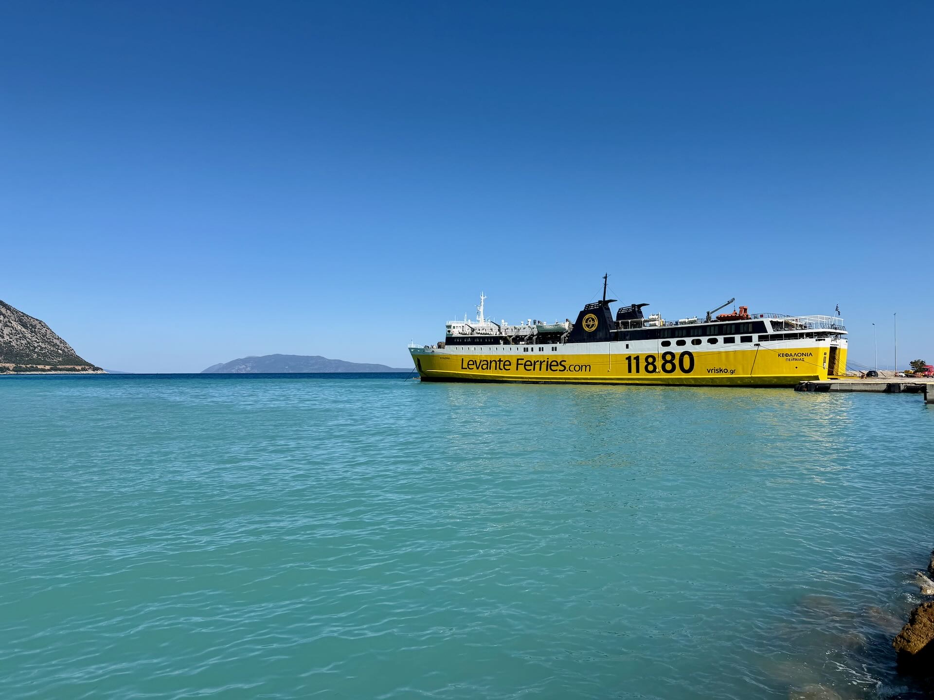 Gelbe Fähre an der Mole in türkisfarbenem Wasser, dahinter Berge