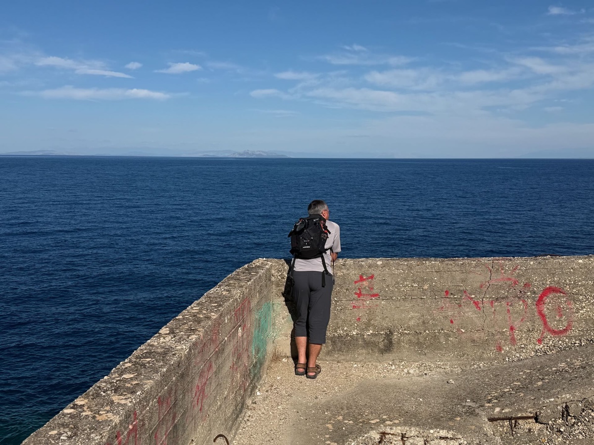 Eine Person steht auf einer bemalten Betonmauer am Meer und schaut aufs Wasser