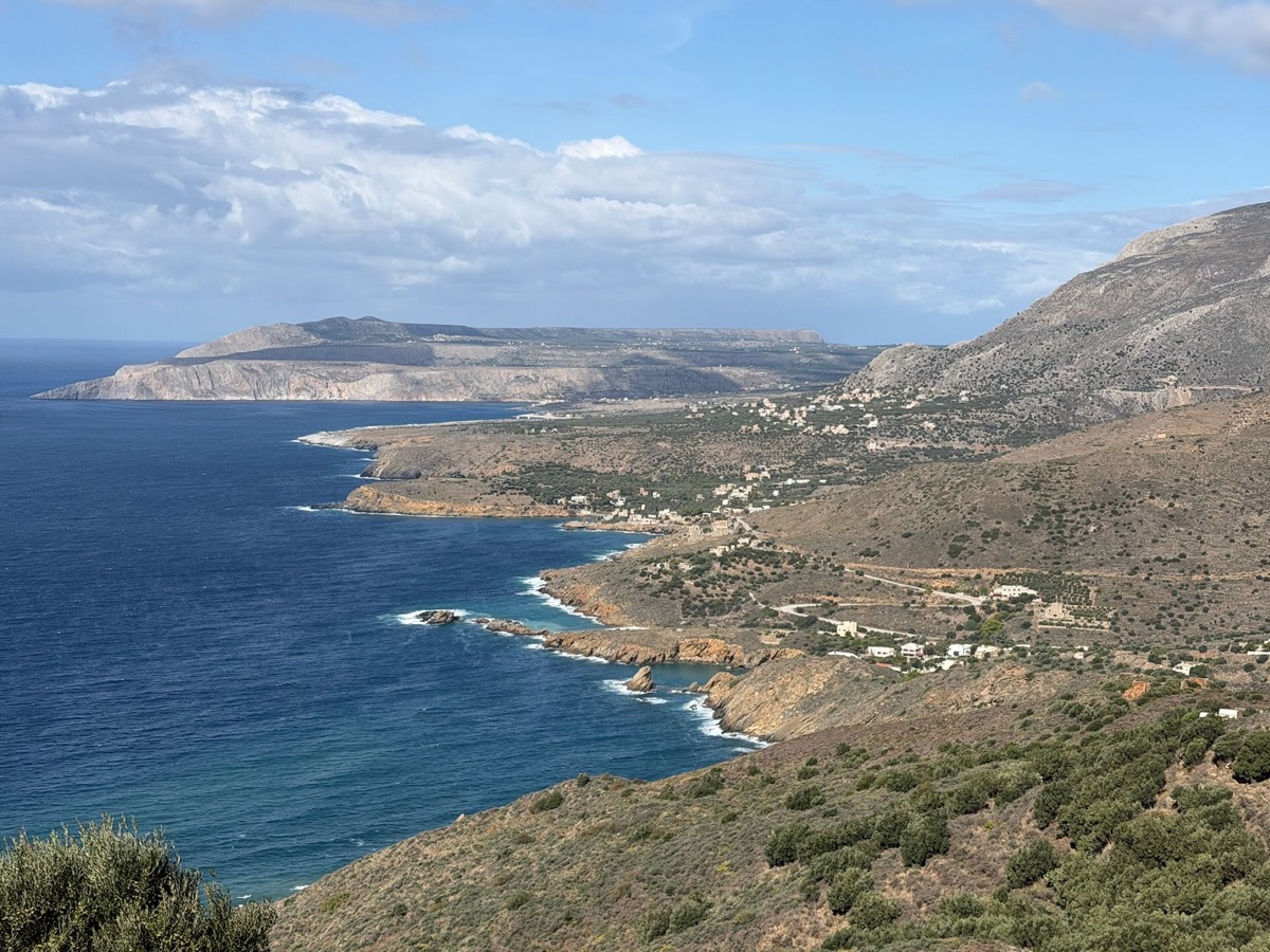 Blick von oben auf eine Küste mit tiefblauem Meer und einem Dorf zwischen Bergen